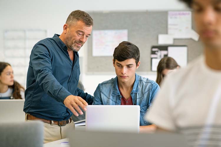 Professor assisting student with laptop in classroom.