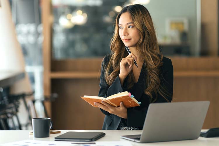 Business Asian woman taking notes on a notebook, and working with a computer.