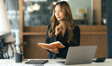 Business Asian woman taking notes on a notebook, and working with a computer.