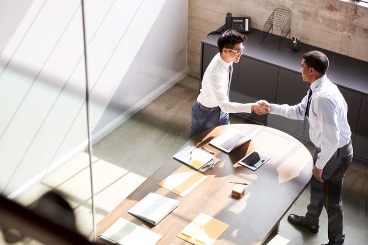 Two businessmen standing in the office shaking hands.