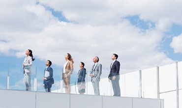 Business people on rooftop balcony looking up at sky.