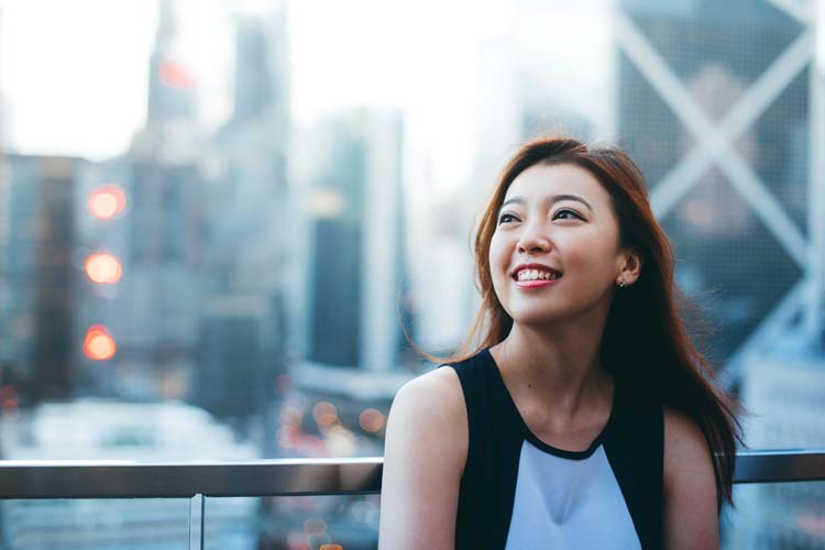 Asian business woman standing on the roof of the financial district and looking up to the sky happily.