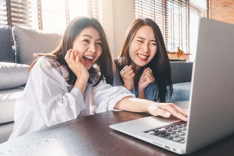 Two happy Asian women using laptop at home.