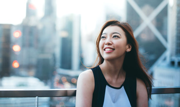 Asian business woman standing on the roof of the financial district and looking up to the sky happily.