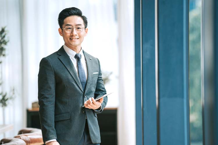 Asian Chinese Businessman looking at camera smiling standing in front of window in conference room.