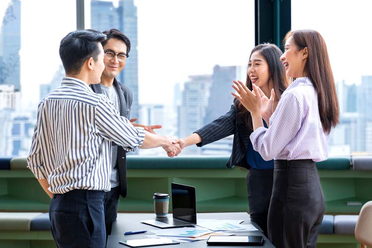 Asian leader congratulates teammate for outstanding team performance in modern office.