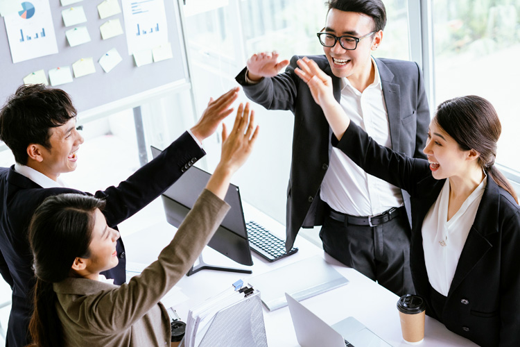 Asian business professionals high fives in their office environment.