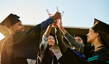 A group of cheerful people at graduation, holding certificates up together and celebrating success.