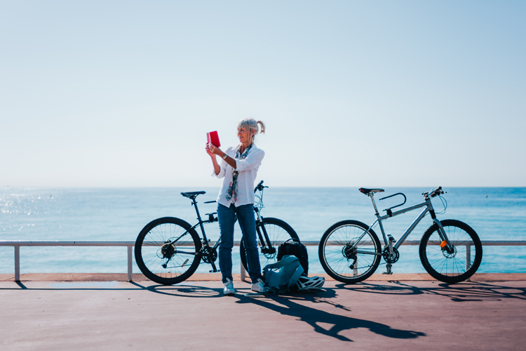 A woman photographing next to her bicycle on a coastal trail.