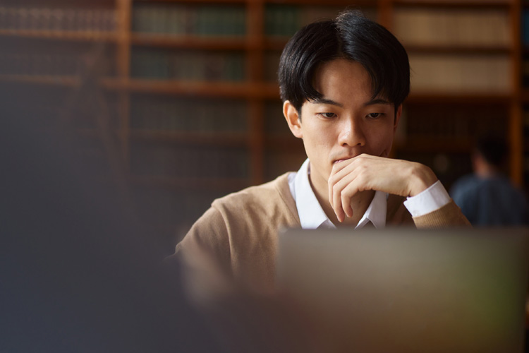 Asian college student using laptop while studying in library.