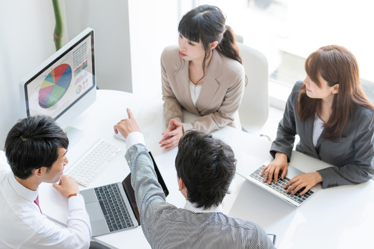 Four professionals discussing at a table with laptops and a pie chart.