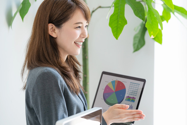 Asian woman presenting financial data on a laptop, smiling, in office setting.