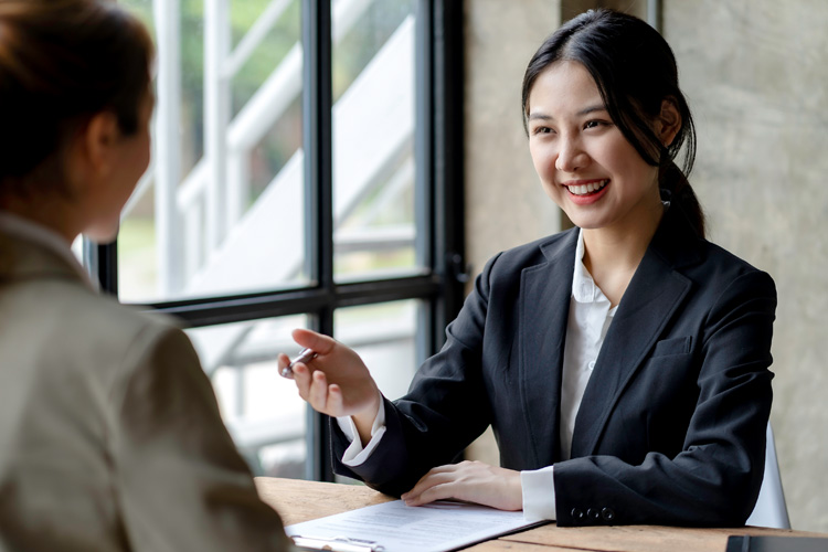 Smiling Asian businesswomen talking to colleague and exchanging ideas together at office.