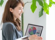 Asian woman presenting financial data on a laptop, smiling, in office setting.