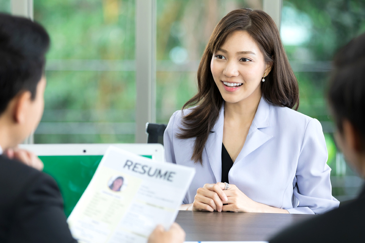 A woman smiles during a job interview, discussing a resume with candidates.