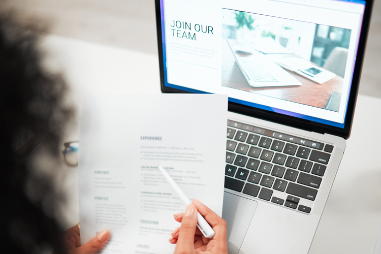 HR with CV, laptop with hiring news on company website and recruitment in office.