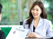 A woman smiles during a job interview, discussing a resume with candidates.