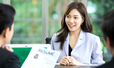 A woman smiles during a job interview, discussing a resume with candidates.