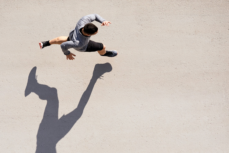 An aerial view of a runner in motion, casting a long shadow on the ground.