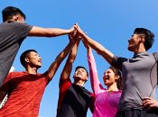 A group of five friends celebrating victory with high-fives against a clear blue sky.