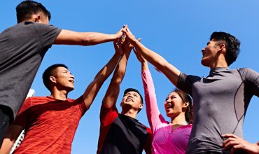 A group of five friends celebrating victory with high-fives against a clear blue sky.