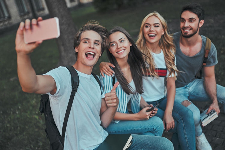 Group of four young friends taking a selfie outdoors, smiling happily.