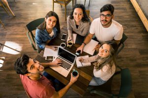 Five young students studying together at a table with laptops and coffee.