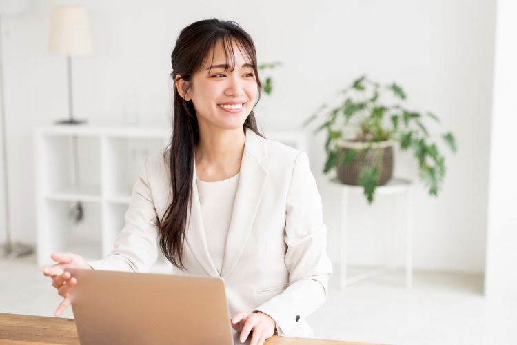 Young Asian businesswoman in a blazer sits at a desk with a laptop, looking engaged.