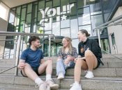 Three students sitting on the steps outside the Your SU building at the University of Sunderland.