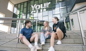 Three students sitting on the steps outside the Your SU building at the University of Sunderland.