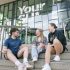 Three students sitting on the steps outside the Your SU building at the University of Sunderland.