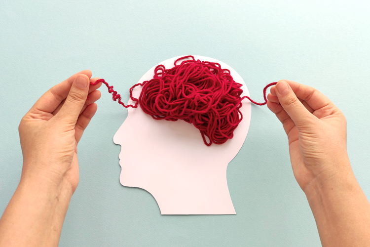 Hands manipulating red yarn on a paper silhouette of a head.
